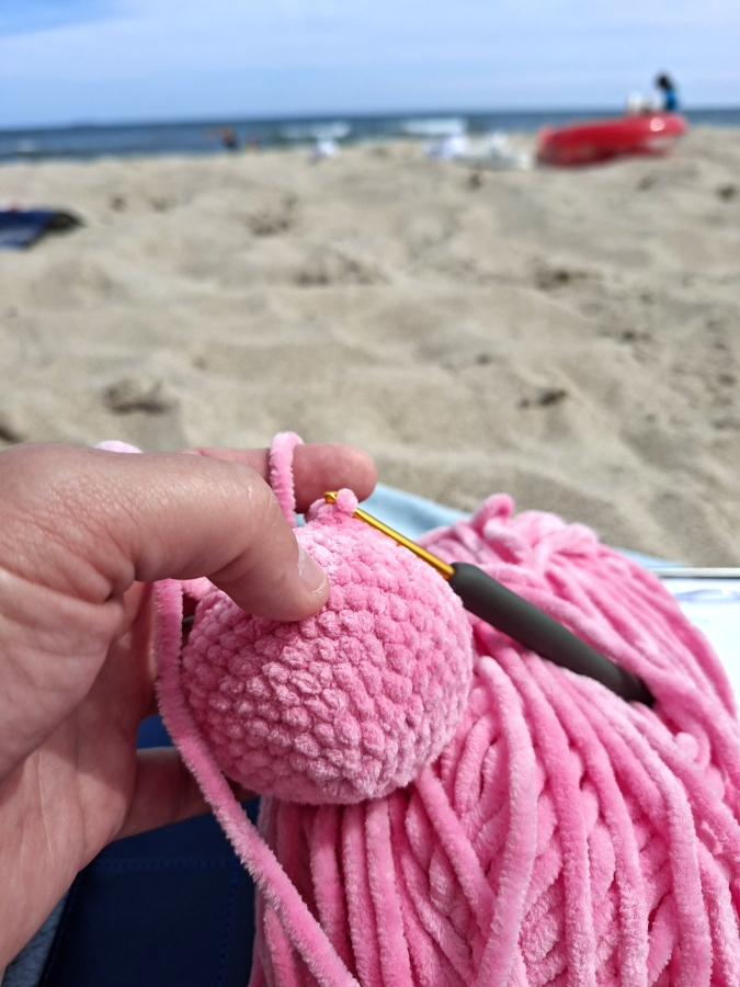 Eine Person sitzt am Strand und häkelt.
